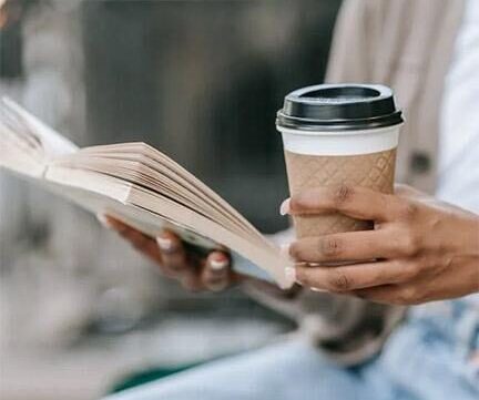 Person holding book and coffee cup